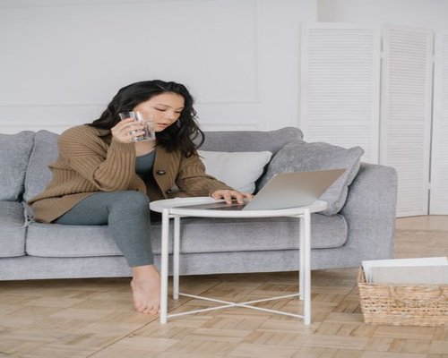 Woman holding a glass of water looking away from her laptop